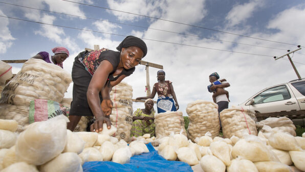 a Nigerian woman bends over bags of produce in a market
