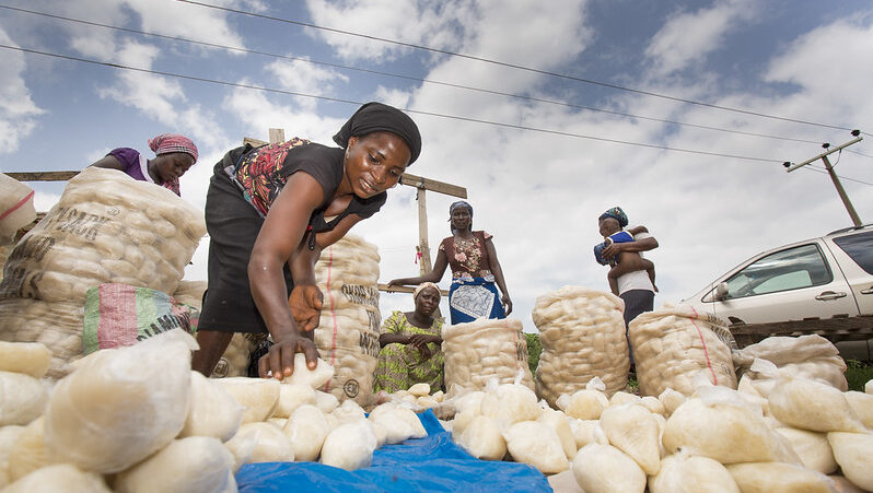 a Nigerian woman bends over bags of produce in a market
