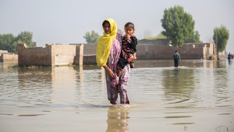 A woman ankle-deep in floodwater carries a girl