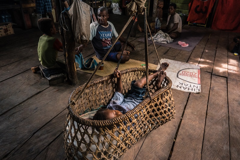 A child in Indonesia inside a basket with familiy members surrounding him.
