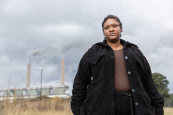 Pascaline Mazibuko standing outside while a coal-fired power plant operates in the background.