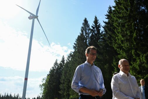 German Chancellor Olaf Scholz and lor Olaf Scholz and North Rhine-Westphalia state premier Hendrik Wuest standing beneath a wind turbine. Germany set to miss net zero by 2045 target, official report says.