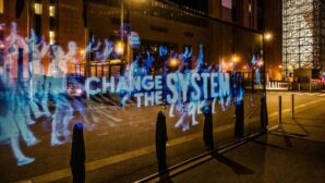 A hologram in a dark streat saying "change the system"