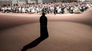 a woman casts a long shadow on the edge of a hall full of Cop28 delegates